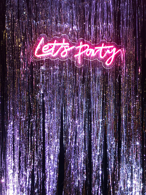 Glitzernder Hintergrund mit Neon-Schriftzug 'Let's Party' – perfekte Kulisse für ausgelassene Feiern